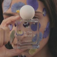 Frau mit lila Blumen im Gesicht hält den Flakon von “In This World – EdP” von Liis in 50ml